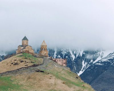 Medieval church on grassy hilltop surrounded by majestic mountains